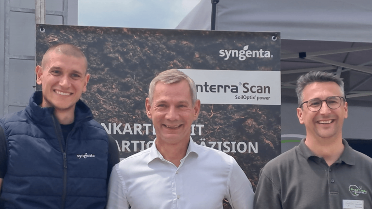 Drei lächelnde Männer vor einem schwarzen Firmenbus mit Syngenta-Schriftzug.