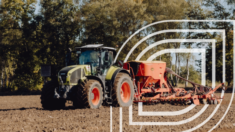 Traktor mit Sämaschine auf Acker, im Hintergrund Bäume und weißes Linienlogo