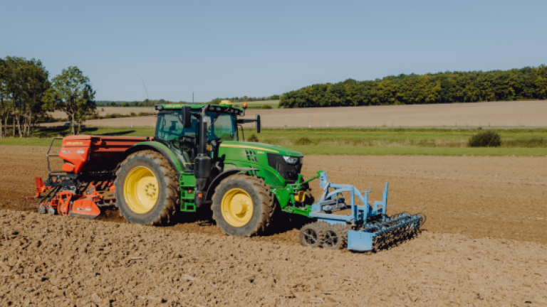 Grüner Traktor mit Sämaschine auf trockenem Feld bei Sonnenschein