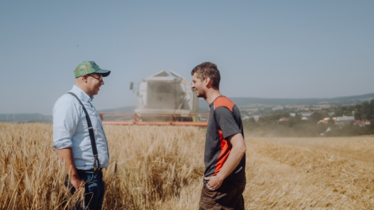 Zwei Männer im Weizenfeld, im Hintergrund ein Mähdrescher und weite Landschaft