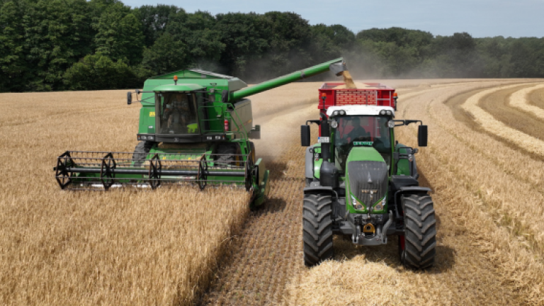Zwei Traktoren ernten Weizenfeld; Staubwolke, grüne und rote Maschinen nebeneinander.