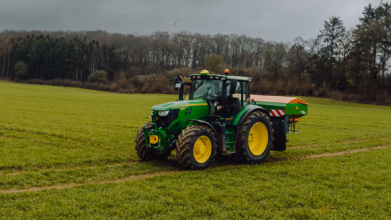 Grüner Traktor mit Anhänger auf grünem Feld unter grauem Himmel