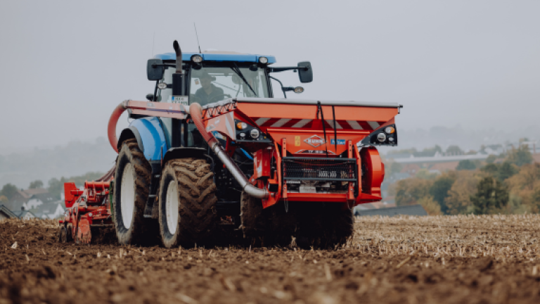 Roter Traktor pflügt ein Feld unter grauem Himmel.